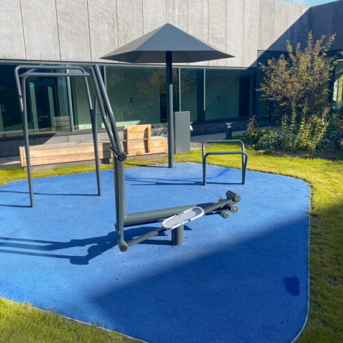 Outdoor workout equipment in courtyard. Cross trainer, pullup bar and parasol.
